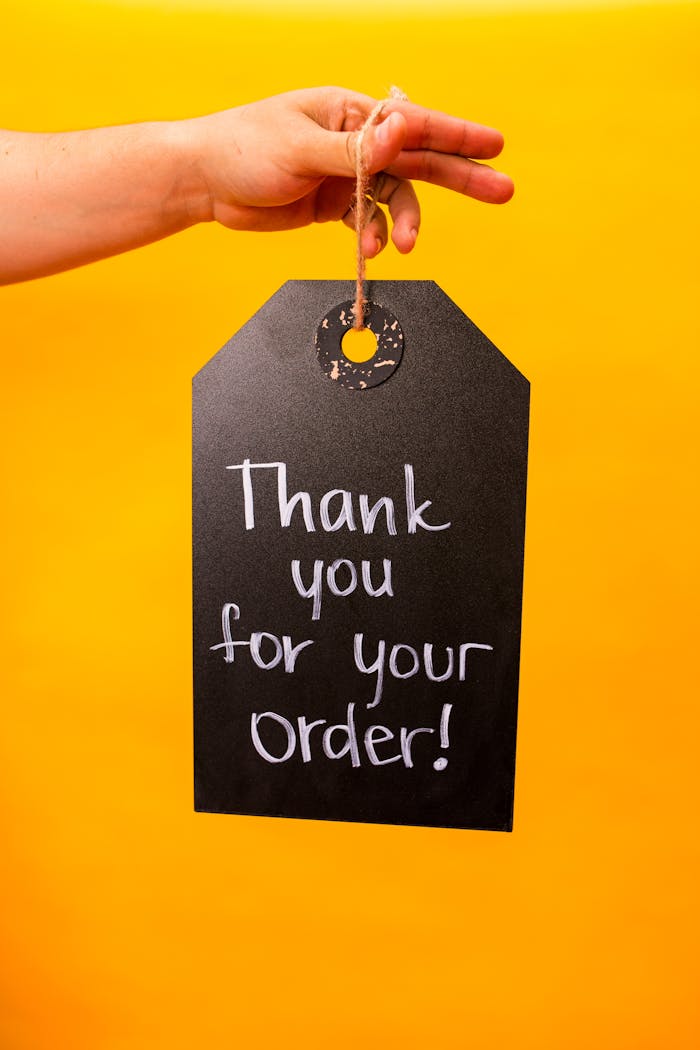 Hand holding a chalkboard with Thank you for your order! written on it, set against a vibrant yellow background.